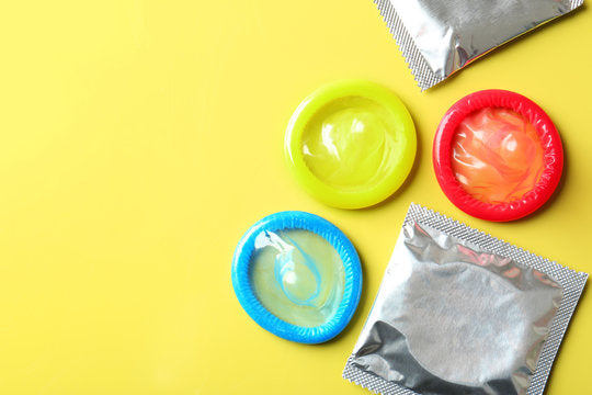 Préservatifs colorés ouverts et emballages en aluminium sur fond jaune.