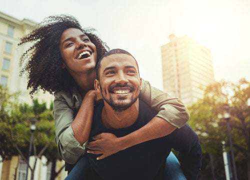 Couple heureux en ville, la femme sur le dos de son partenaire riant ensemble lors d’un moment complice en plein air dans un environnement urbain.