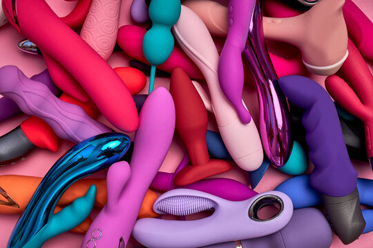 Collection colorée de jouets sexuels pour adultes, dont vibromasseurs et stimulateurs, disposés en vrac sur un fond rose.
