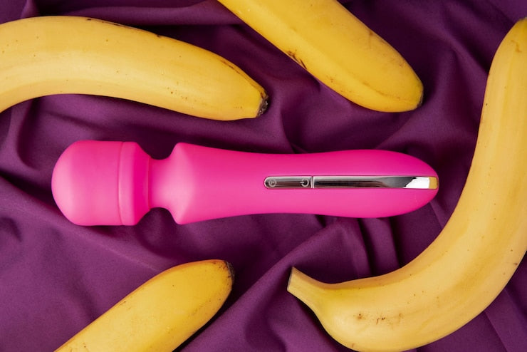 Une vibromasseur rose sur tissu violet entouré de bananes.