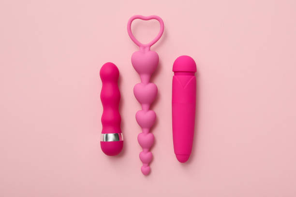 Jouets sexuels roses pour adultes, dont un vibromasseur, un plug anal en forme de cœurs et un stimulateur, disposés sur un fond rose minimaliste.