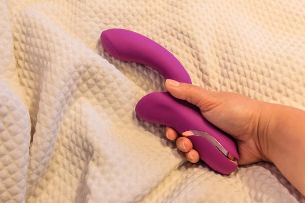 Vibrateur rabbit violet en silicone tenu dans la main sur un fond de couverture blanche.
