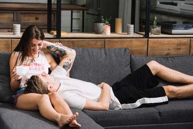Couple détendu sur un canapé, moment complice à la maison, femme tenant une tasse de café.